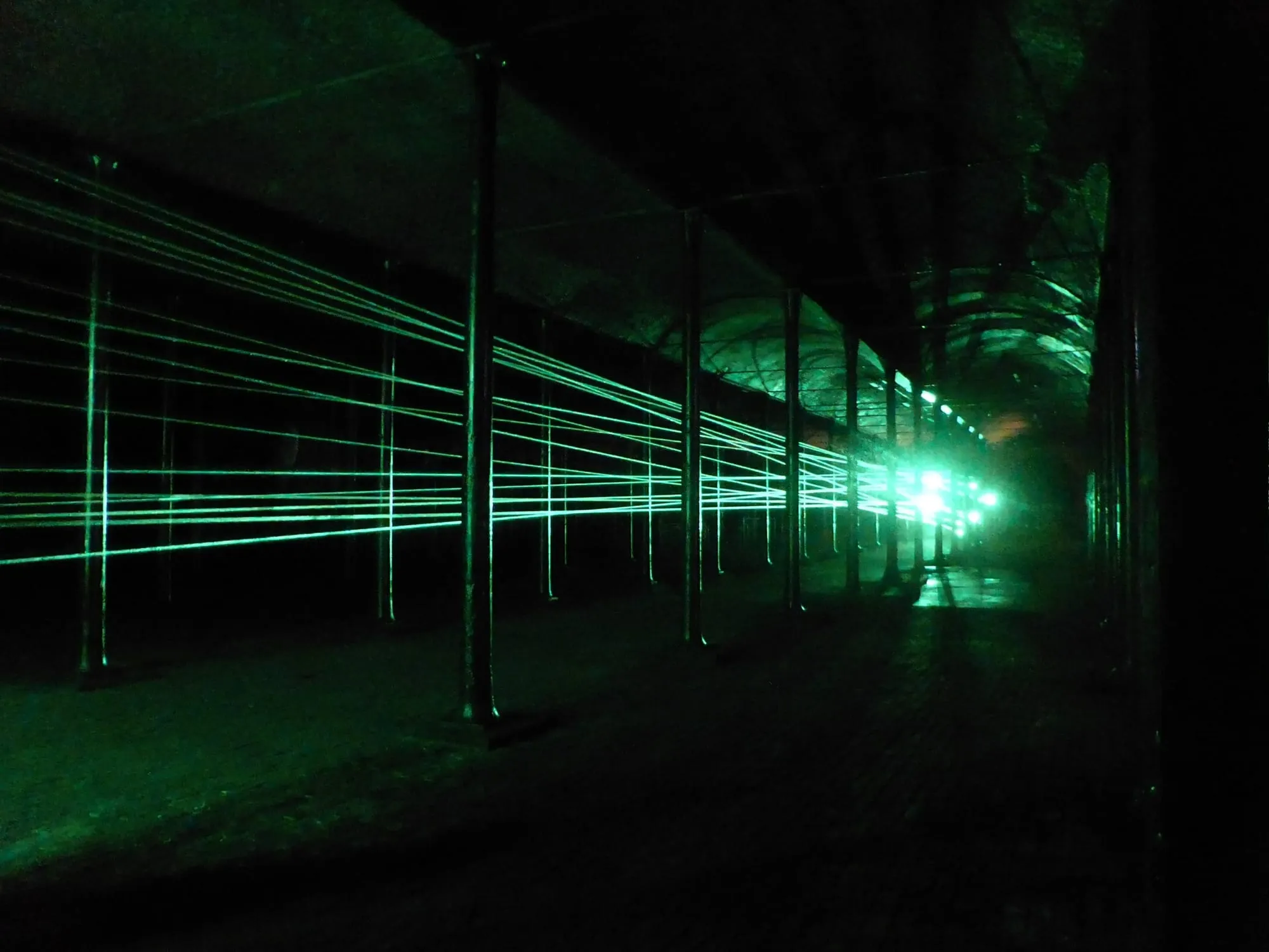 Green laser beams criss-crossing between cast-iron columns in the dark interior of Toxteth Reservoir, part of Rita McBride's installation